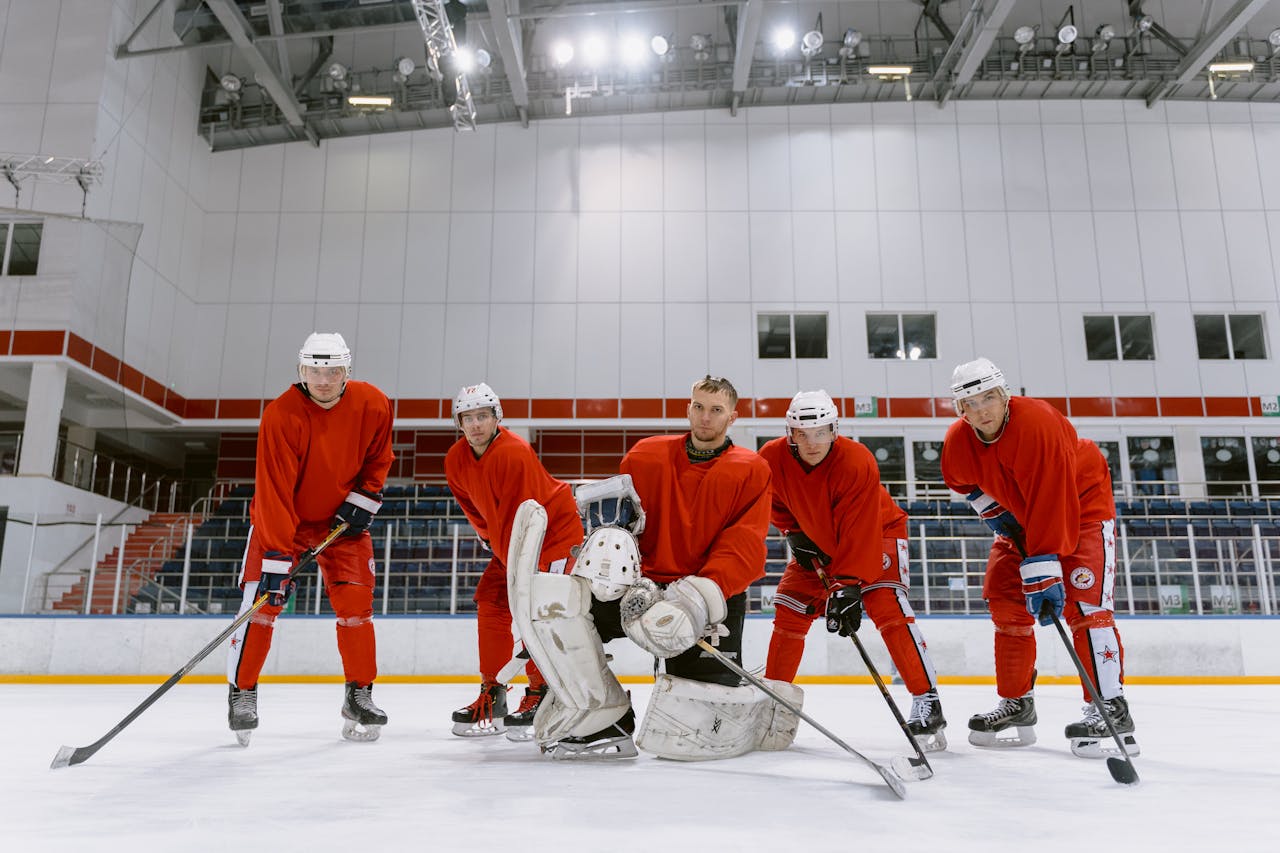 Group of male hockey players in red jerseys posing on an indoor ice rink.